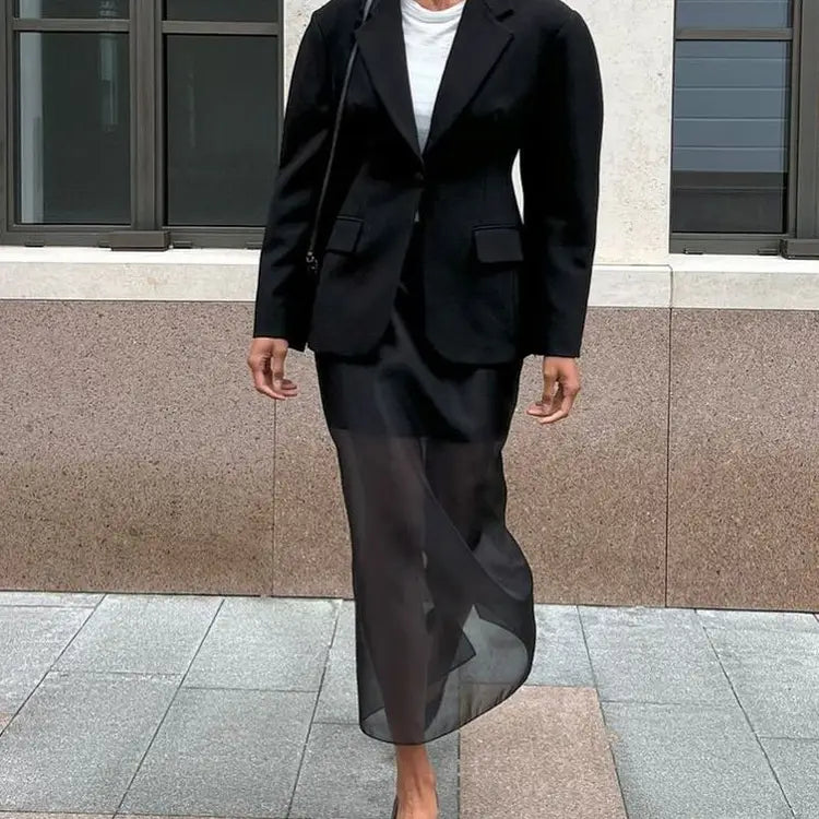 Black blazer with structured shoulders and two front flap pockets paired with a black sheer high waist slit sheath skirt.