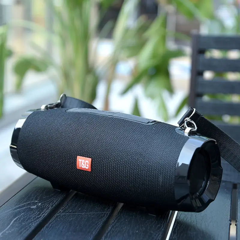 black fabric-wrapped strap wireless bluetooth speaker with glossy black plastic ends and red t&g logo patch designed for portable wireless bluetooth audio use