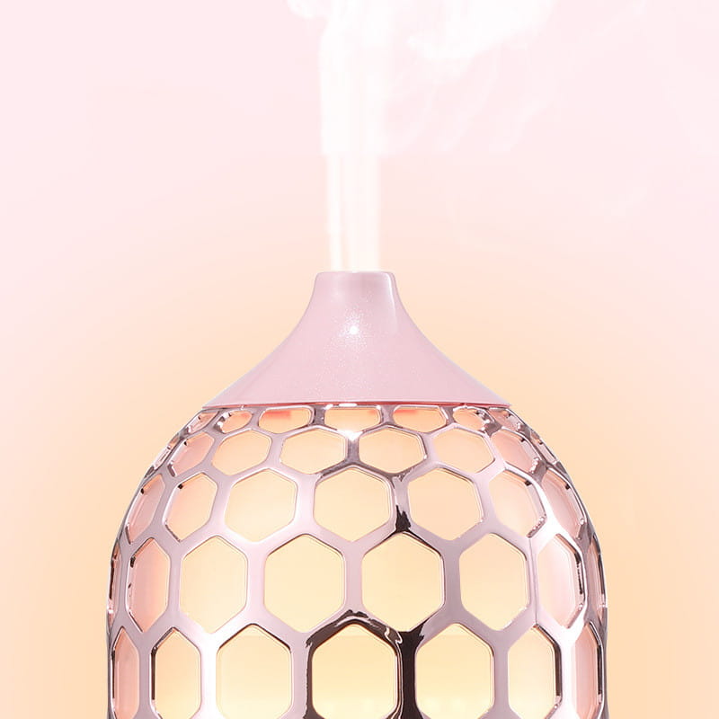 A sleek rose gold asakusa pink aroma diffuser with a honeycomb pattern emitting a gentle mist.