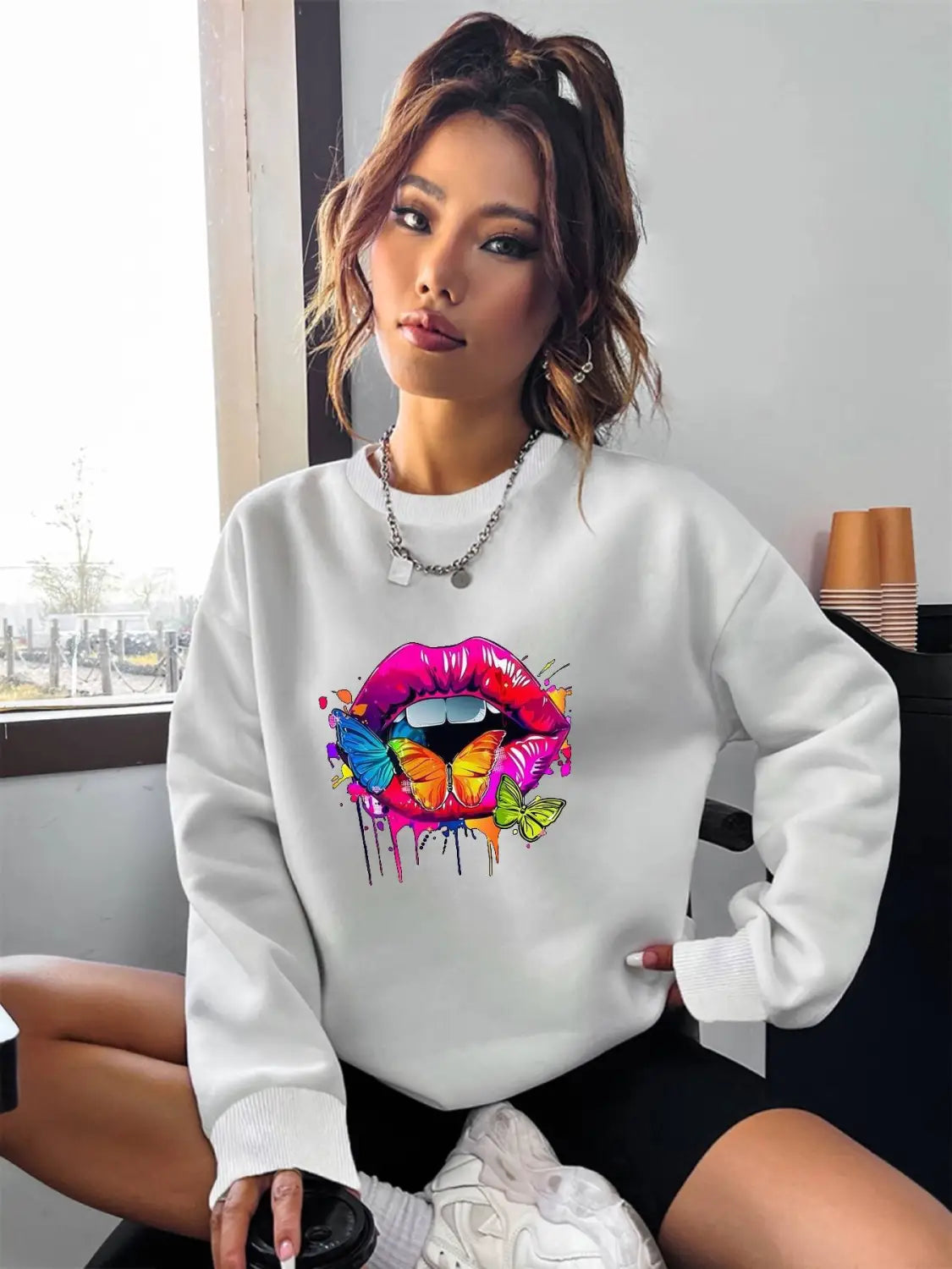 white oversized crew neck sweatshirt featuring a vibrant colorful graphic of lips with butterflies and paint drips
