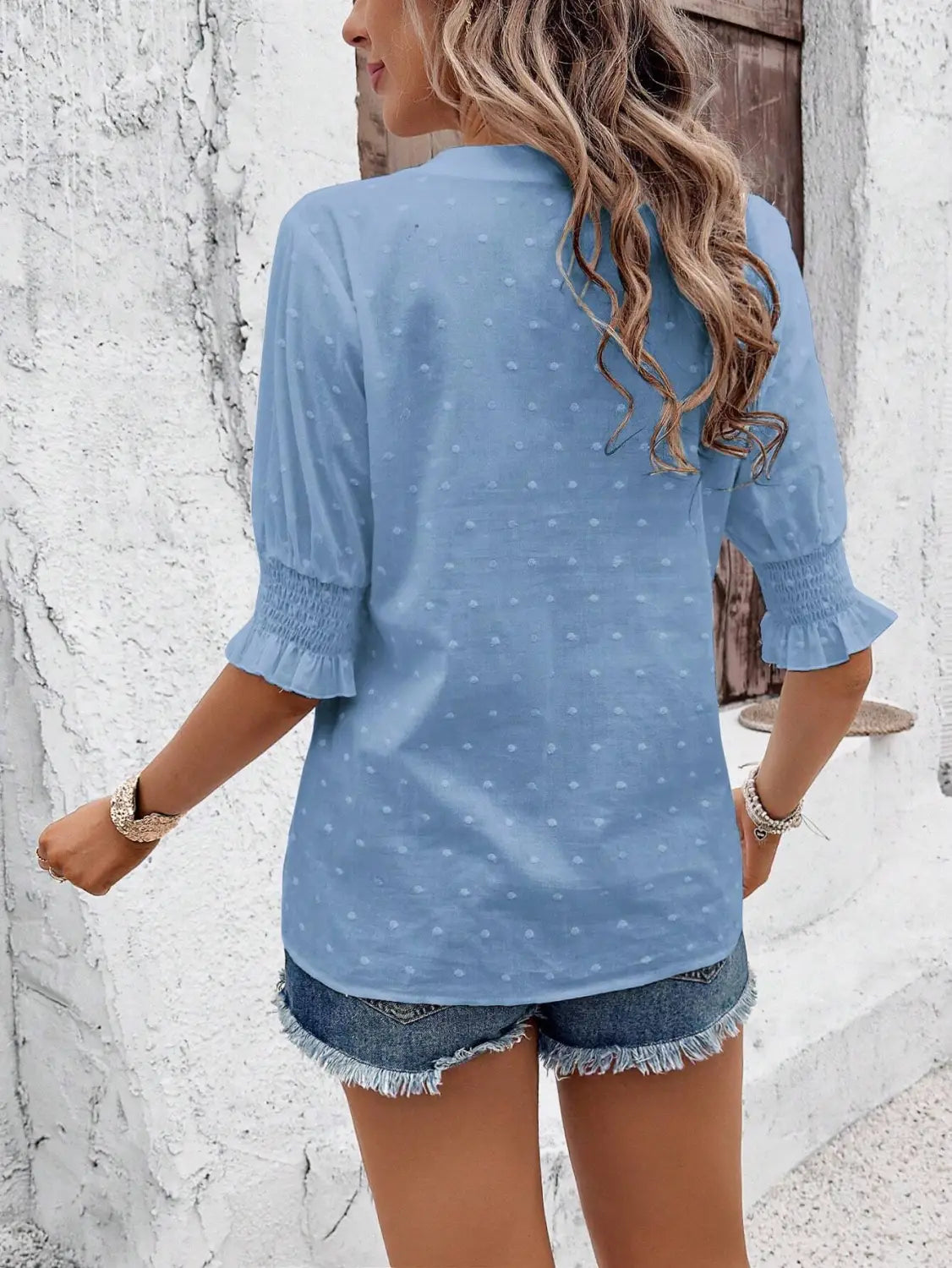 Light blue blouse with subtle white polka dots featuring ruffled three-quarter puff sleeves and a hollow hair ball design.