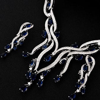 Silver jewelry set featuring a necklace and matching earrings adorned with deep blue sapphire-like stones and sparkling white gemstones in an elegant flowing design, part of the emerald green crystal jewelry zircon collection.