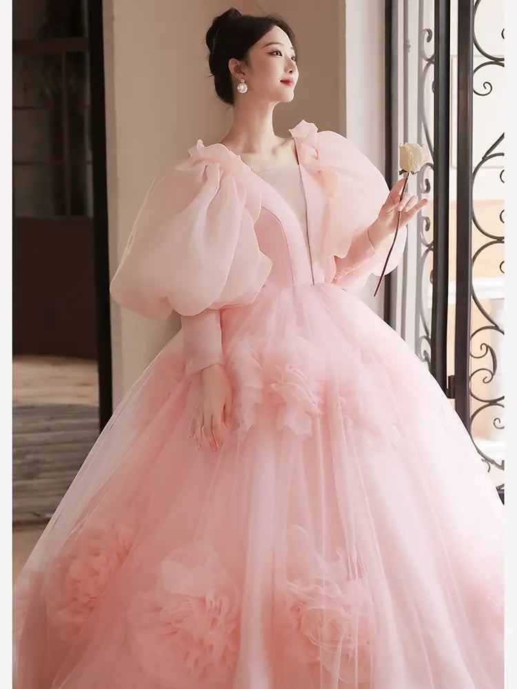 A flowing blush pink high end banquet style host ball gown featuring voluminous puffy sleeves and delicate floral appliqués on the tulle skirt.