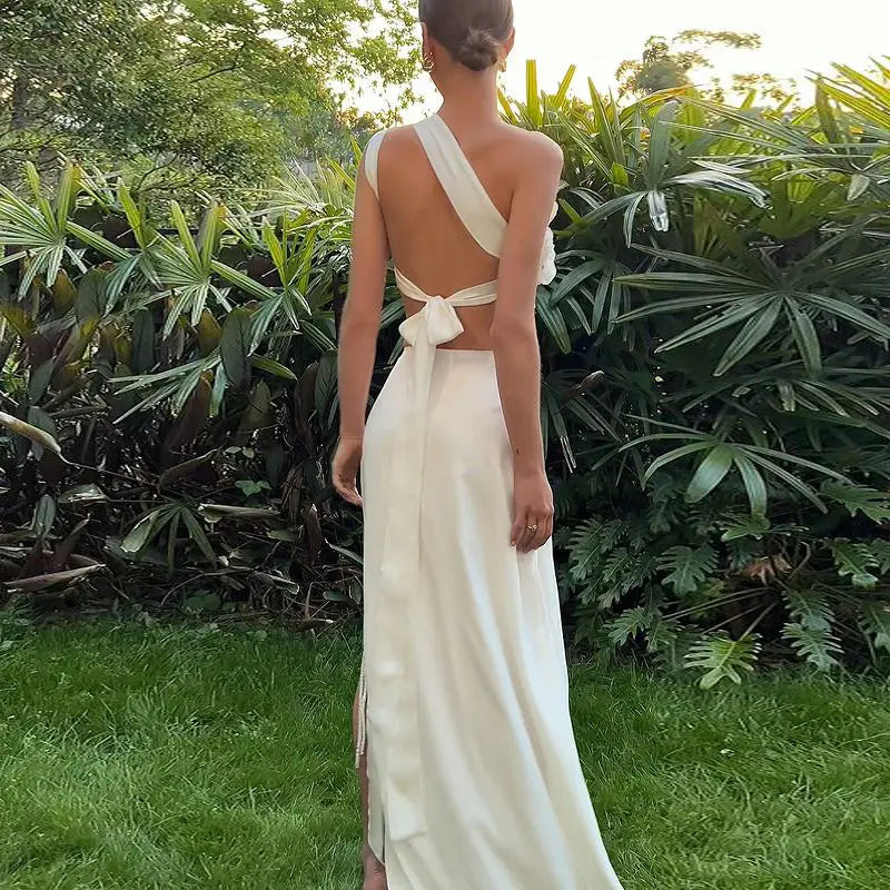 A flowing off-white satin gown with a single-shoulder design and tied-back waist featured as part of a backless sequined lace split skirt suit.