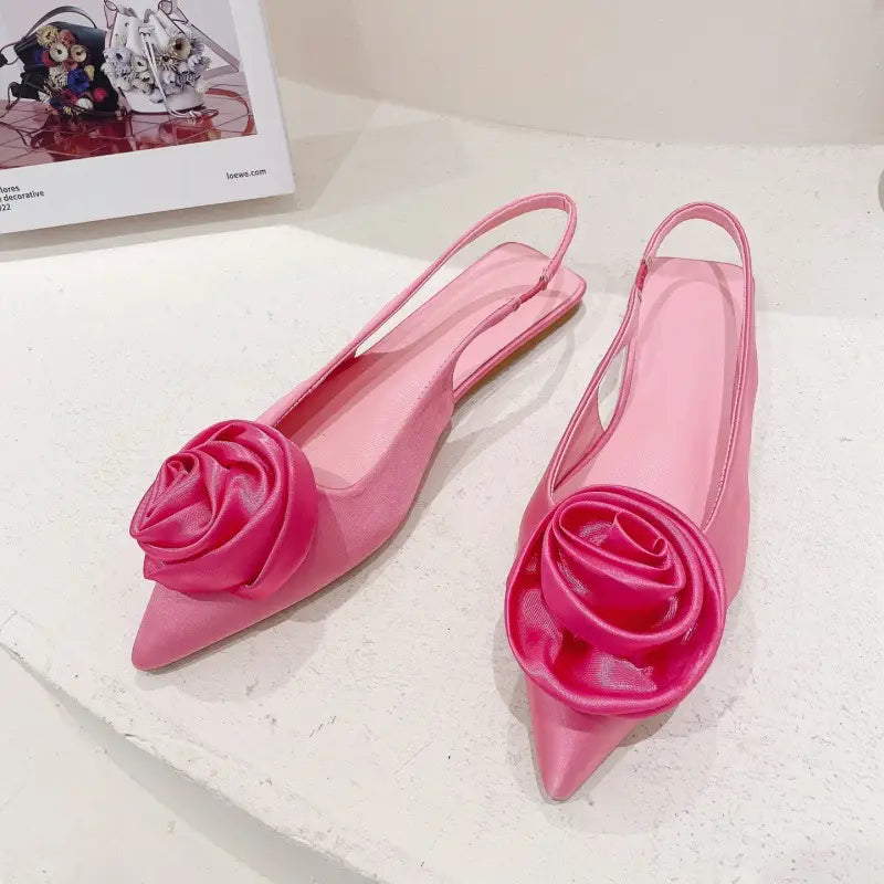 pink satin floral embellished backless flat sandal featuring pink satin slingback flats with a glossy rose embellishment at the toe.