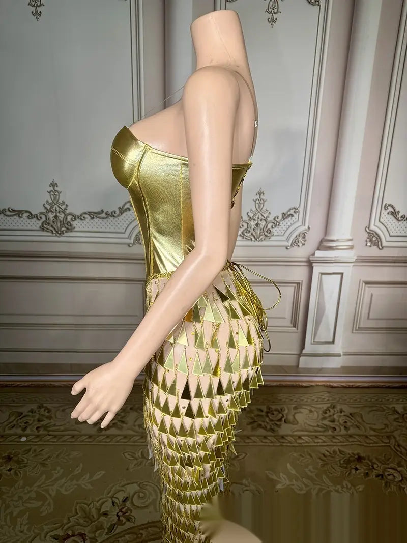 a shimmering gold metallic corset dress featuring a fitted bodice and a lower section with triangular scale-like panels showcasing a golden bright surface bandage metallic mermaid gown with surface bandage design