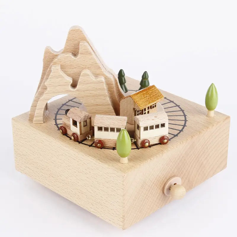 a light-colored wooden diy dancing music box featuring a miniature train with red wheels traveling around an oval track past a mountain, trees, and a house.