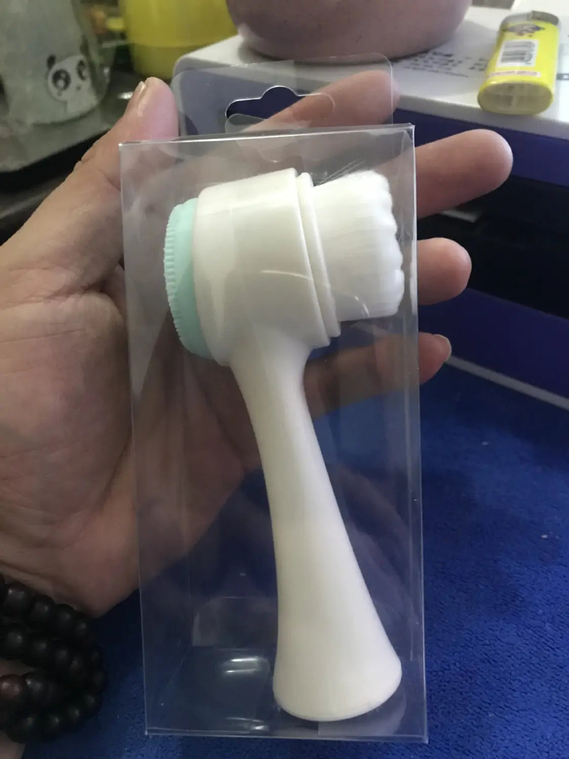 White and light blue dual sided silicone facial cleansing instrument in clear plastic packaging for beauty skin care face wash use.