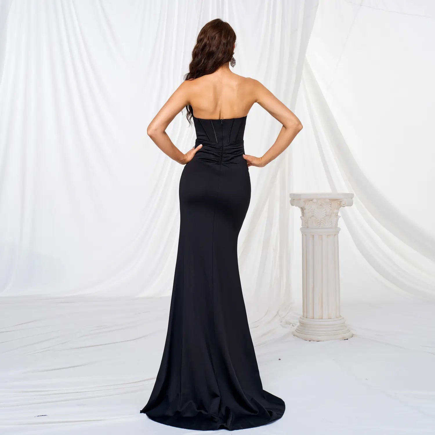 A sleek black satin strapless ruched evening dress featuring a corseted bodice and a long large hem flowing train.