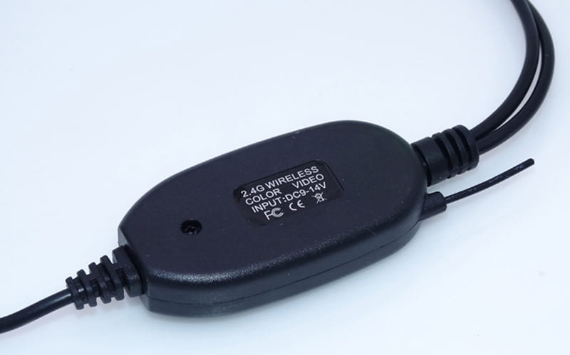 black plastic 2.4g wireless video transmitter with two black cables and dc9-14v input voltage label shown on the back side of a 7 inch display hd wireless suction cup display rearview camera.