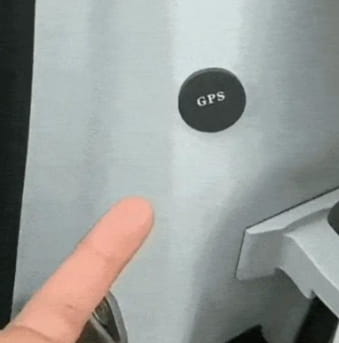 A black circular gps button with white lettering mounted on a light gray surface of a gps car tracker featuring dual microphone recording.