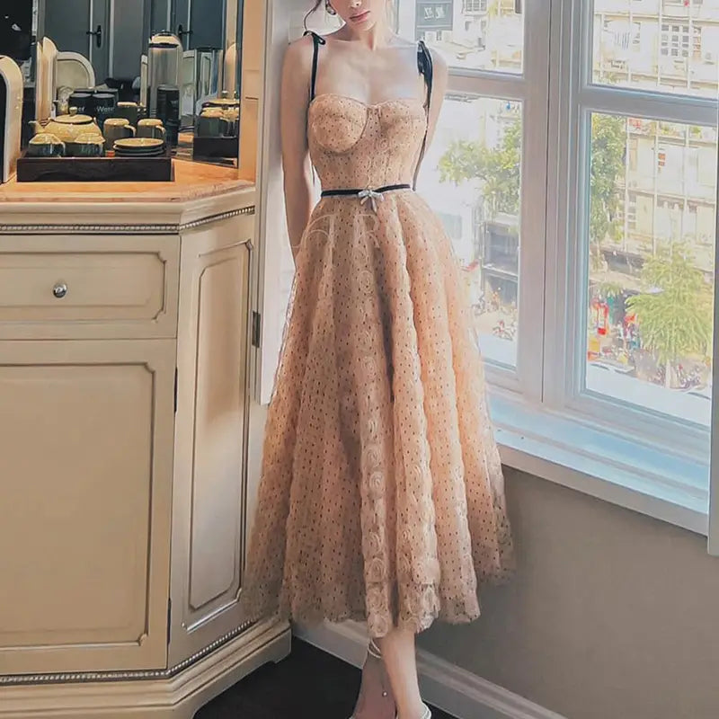 a blush pink lace slim drawstring dress featuring a delicate corseted bodice, thin black straps, and floral embroidery along the midi skirt hemline