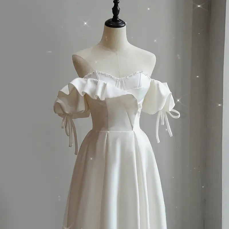 a white satin light wedding dress featuring an off the shoulder design with puffed sleeves tied at the wrist and a beaded neckline for the wedding dress bride
