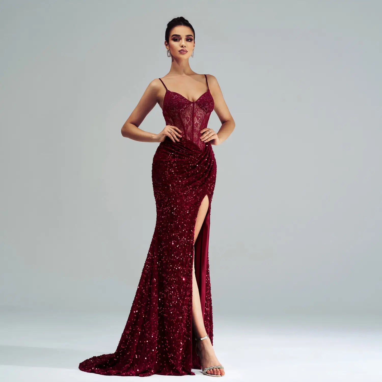 A shimmering burgundy sleeveless sequined high slit evening dress with a lace bodice and spaghetti straps.