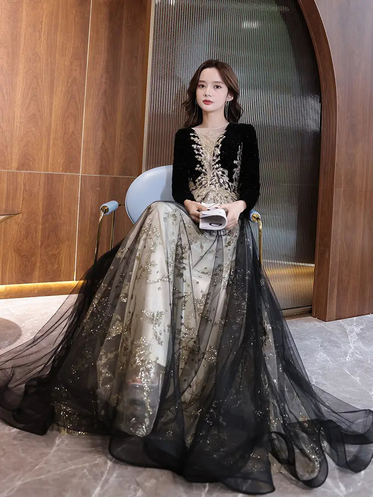 Elegant black moderator long sleeve annual party dress featuring a velvet bodice with black and gold embroidered details and a sheer layered skirt.