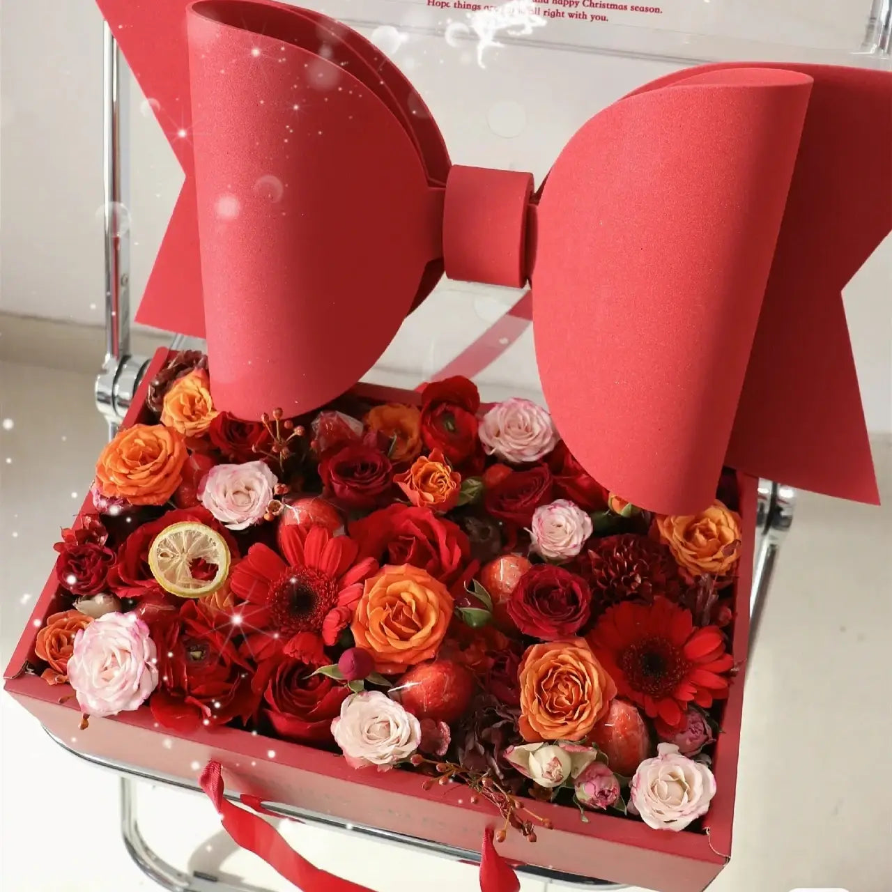 A vibrant red bow knot handheld flower box with a glossy finish features an ornate floral arrangement in a matching pink box with a clear window.