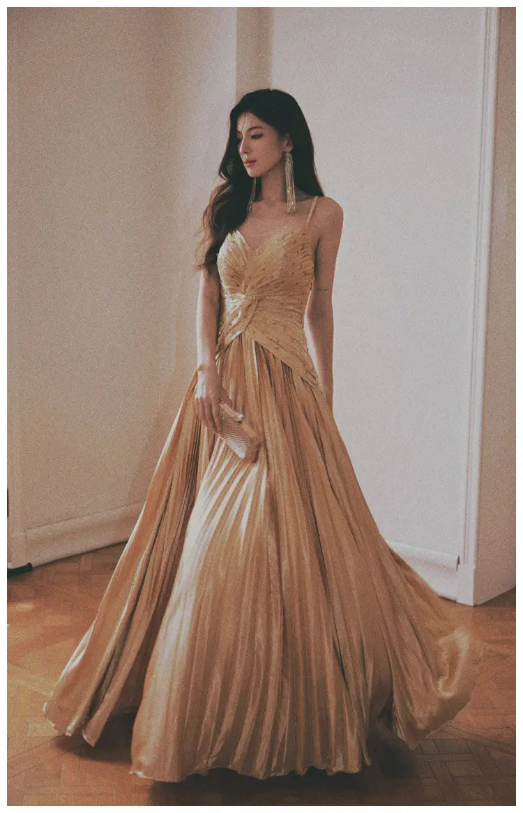 A flowing gold satin heavy industry birthday dress featuring a pleated gown with a fitted bodice and delicate spaghetti straps.