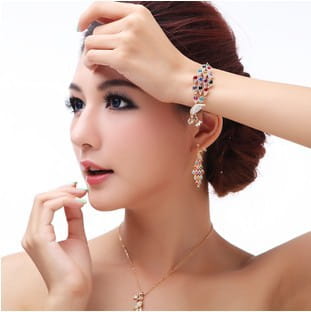 A woman wearing a delicate gold crystal peacock bridal necklace with an ornate pendant complemented by matching earrings and bracelet showcasing the creative crystal peacock bridal jewelry set.