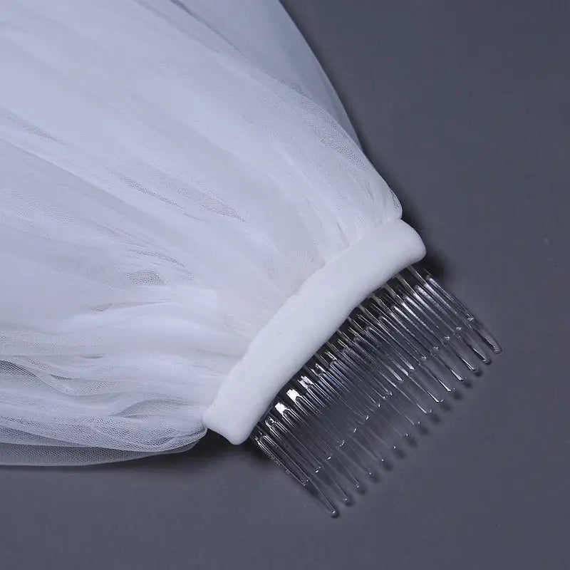 A delicate white tulle bridal wedding veil with a widened tail attached to a clear plastic comb.