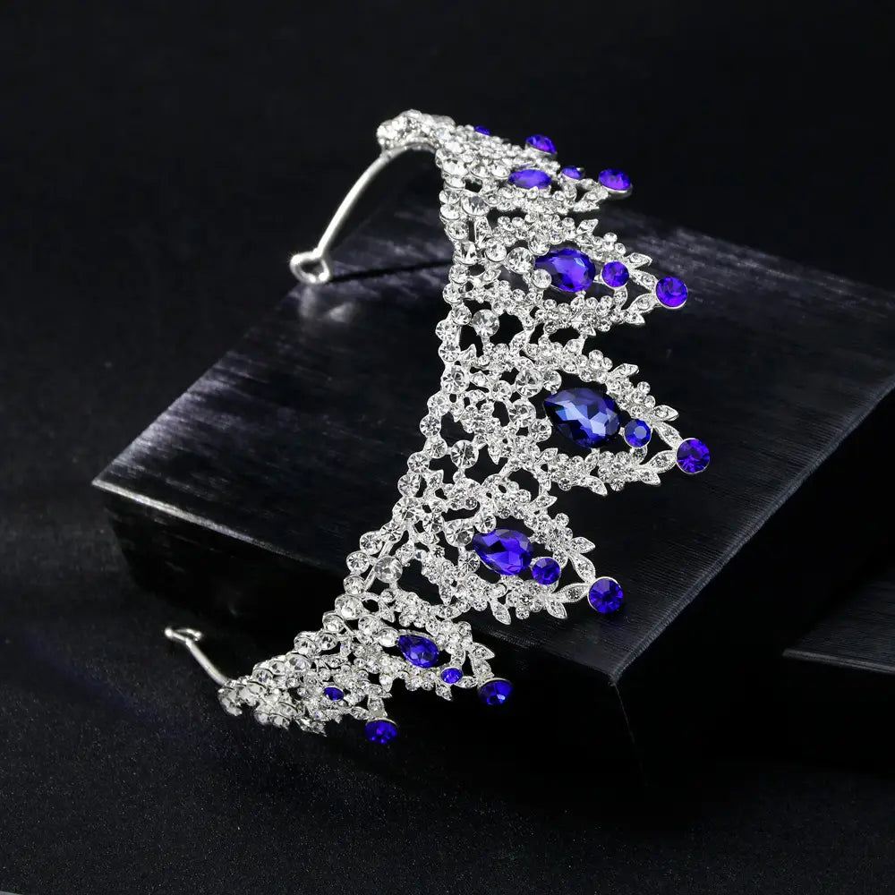a sparkling silver bridal crown european featuring intricate lace-like metalwork with deep blue oval and round rhinestones and smaller clear teardrop crystals.