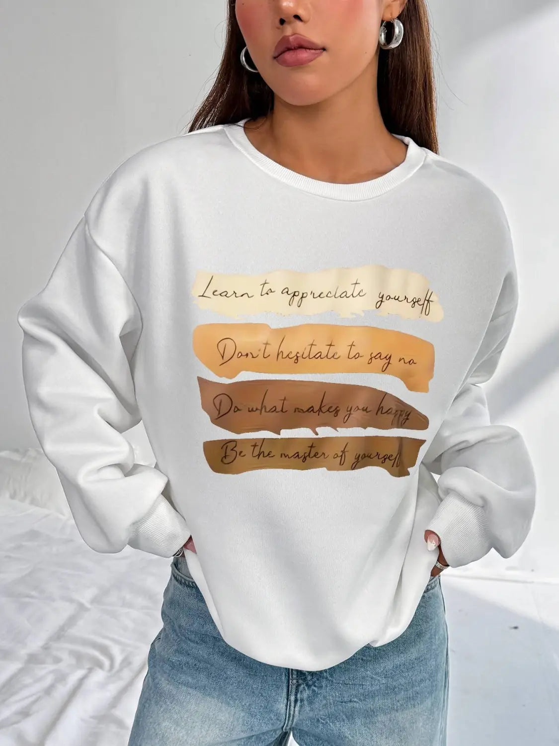 White oversized long sleeve sweatshirt in solid colour featuring a motivational quote printed in brown cursive text on layered textured beige and tan horizontal bands ideal for daily wear.