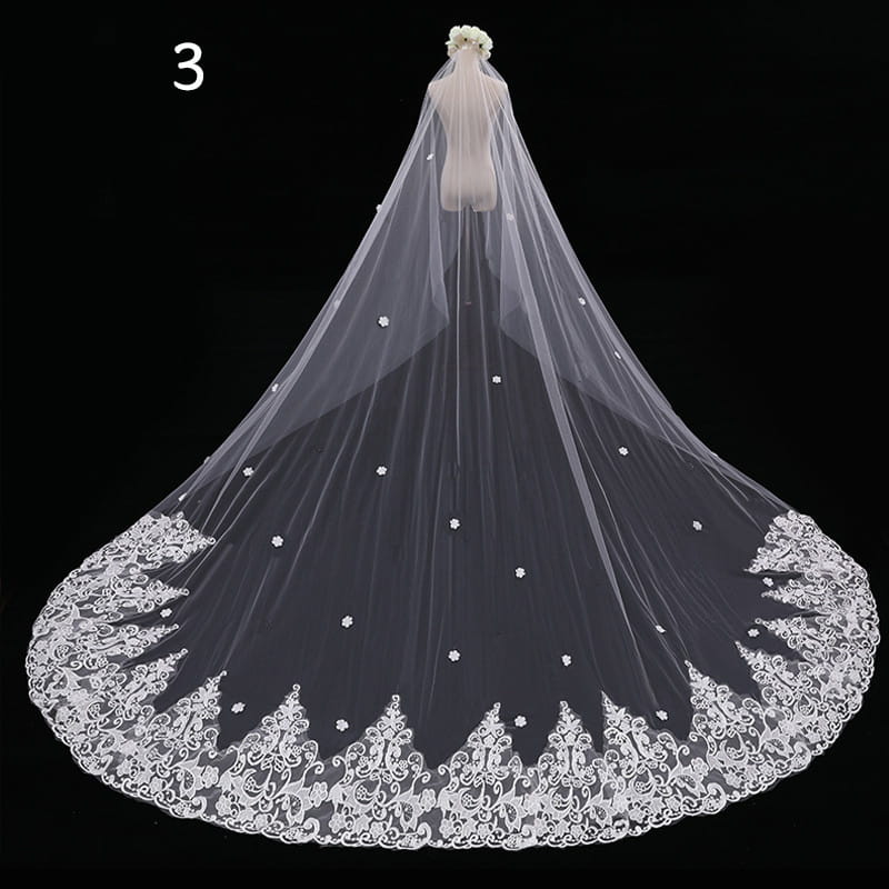 a delicate white lace wedding veil with intricate floral embroidery and small embellishments along the hem in a long meters wide wide style