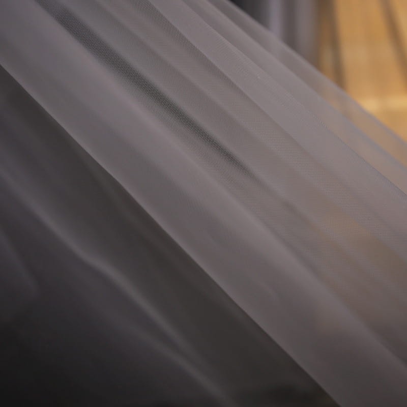 Delicate white tulle fabric with a soft translucent texture and subtle sheen featured in a lace wedding dress with trailing floral bridal veil.