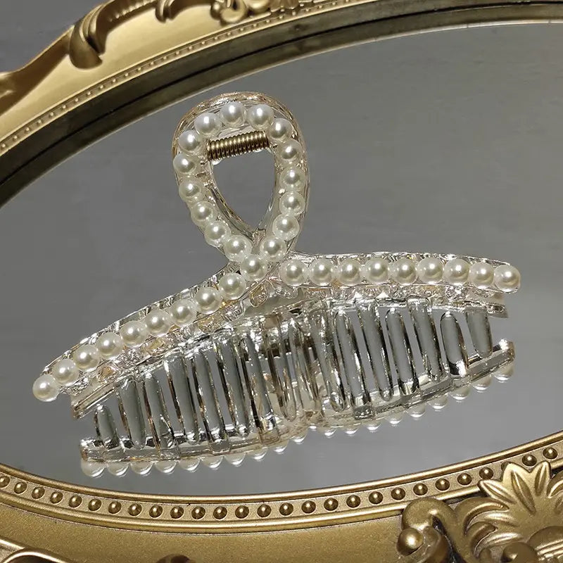 A transparent pearl grab clip with a silver-toned metal frame, pearl embellishments, and decorative rhinestone bow, offering a gentle and elegant clip gentle transparent design.