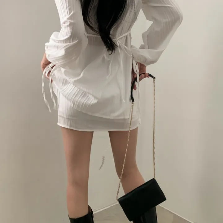 black chain-strap clutch bag complementing a white ribbed long sleeve shirt dress with tie waist
