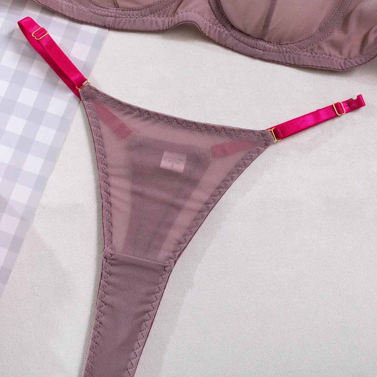 A delicate mauve mesh thong with vibrant fuchsia satin straps and gold-toned hardware featured in a lavender and pink see-through two-piece set made from comfortable fabric.
