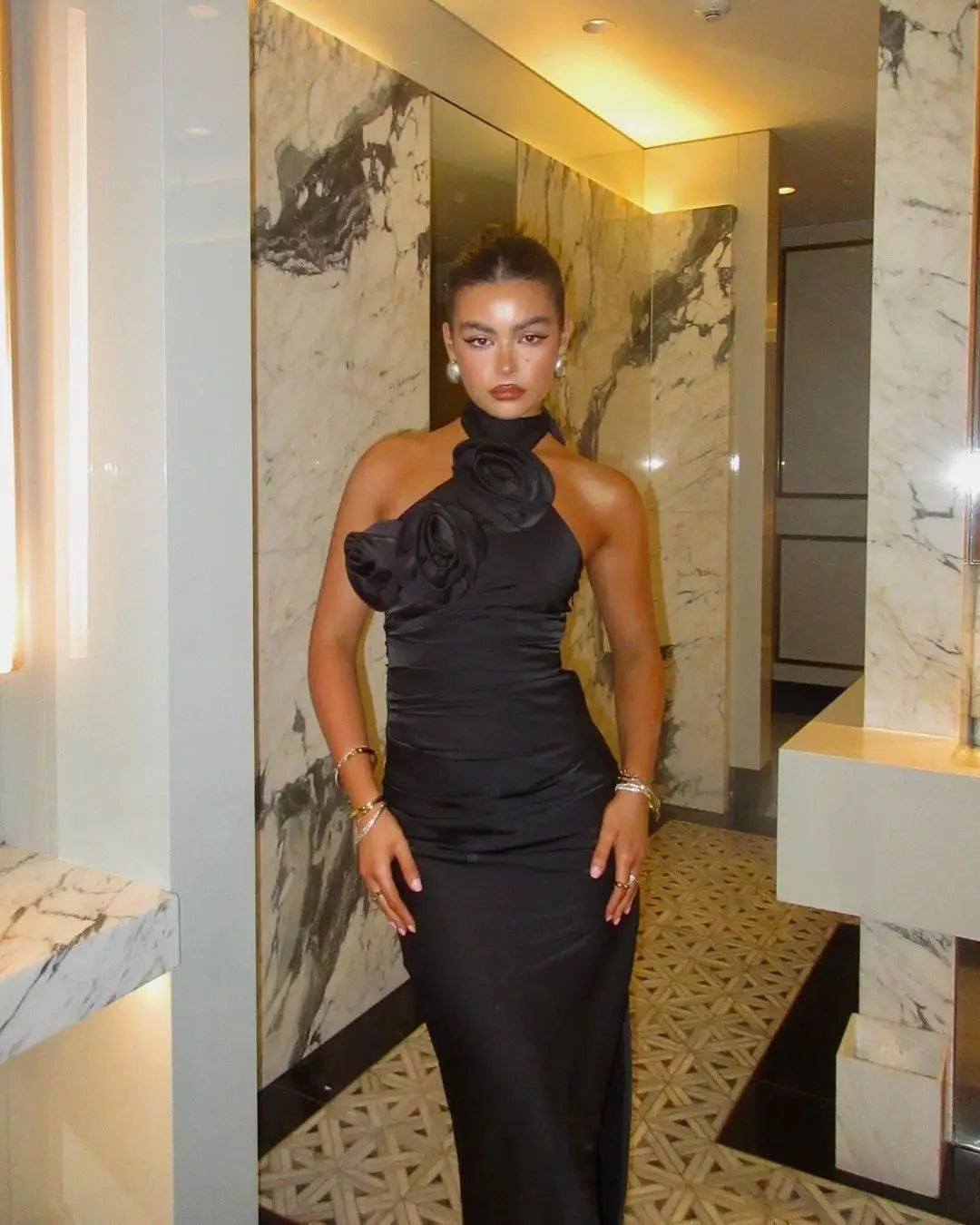 black satin one-shoulder gown featuring a large ruffled white ribbon flower accent at the neckline in a ribbon flower halter style
