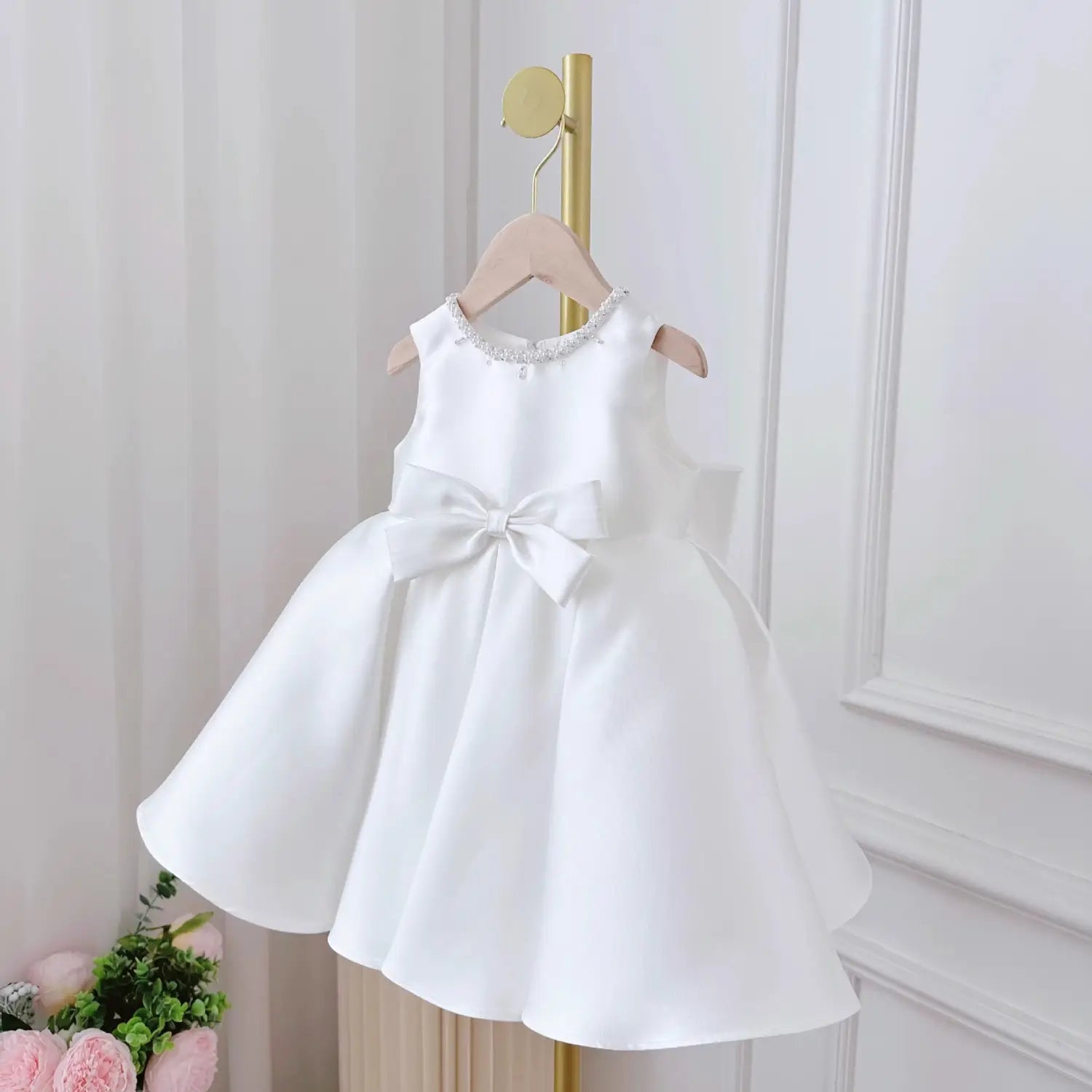 White satin sleeveless toddler baby dress white with a beaded neckline and a large bow at the waist in white classic style.