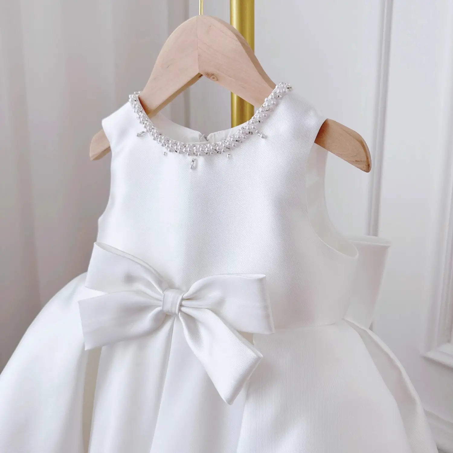 A white satin baby dress white classic style featuring long sleeves, a beaded neckline, and a large bow at the waist.