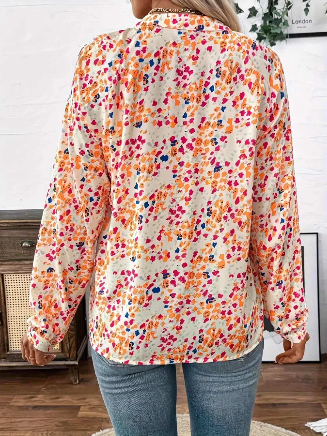 A woman wearing a cream-colored lantern sleeve floral print v neck blouse featuring vibrant orange pink and blue hues.