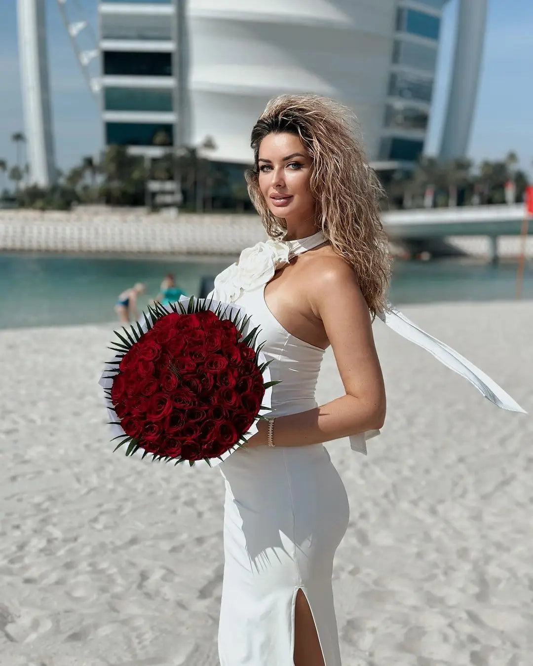 a lush vibrant red rose bouquet with dark green thorns and a white ribbon accent complements the satin white ribbon flower halter gown style white ribbon detail.
