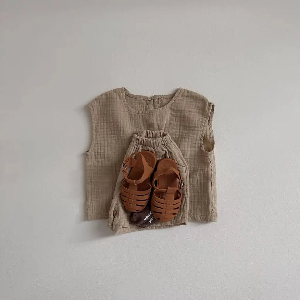tan children’s sandals with a woven strap design complementing a breathable vest shorts set made of cotton muslin for comfortable summer wear