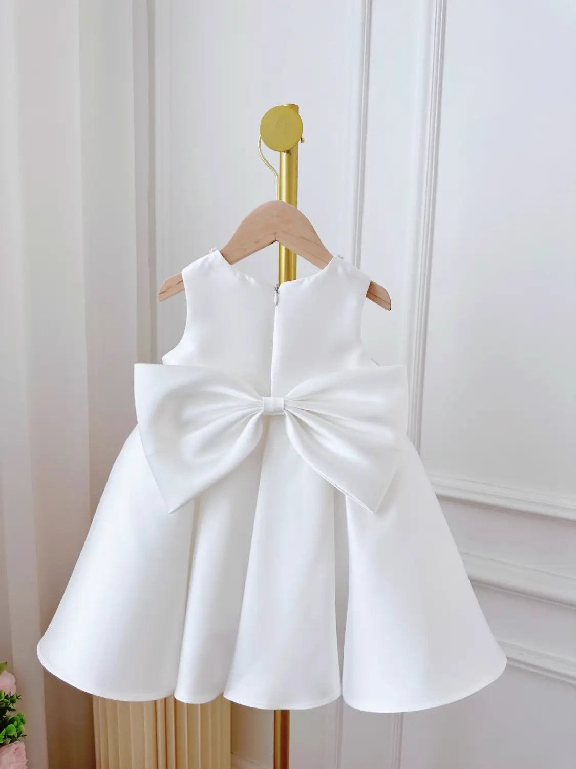 white sleeveless baby dress white classic style with a large satin bow at the back hanging on a wooden hanger