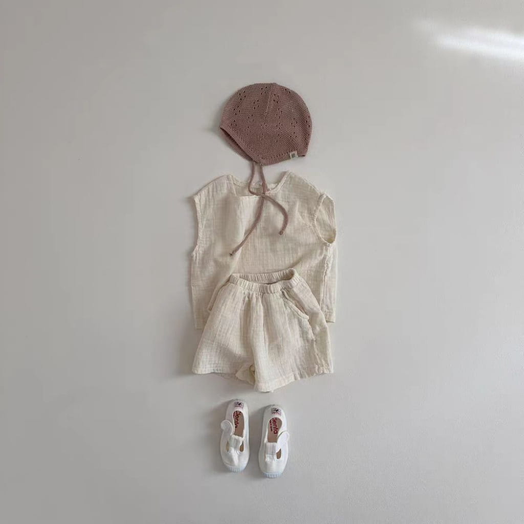 a soft dusty rose knitted baby bonnet with a delicate lace pattern and matching ties paired with a breathable vest shorts set made from cotton muslin