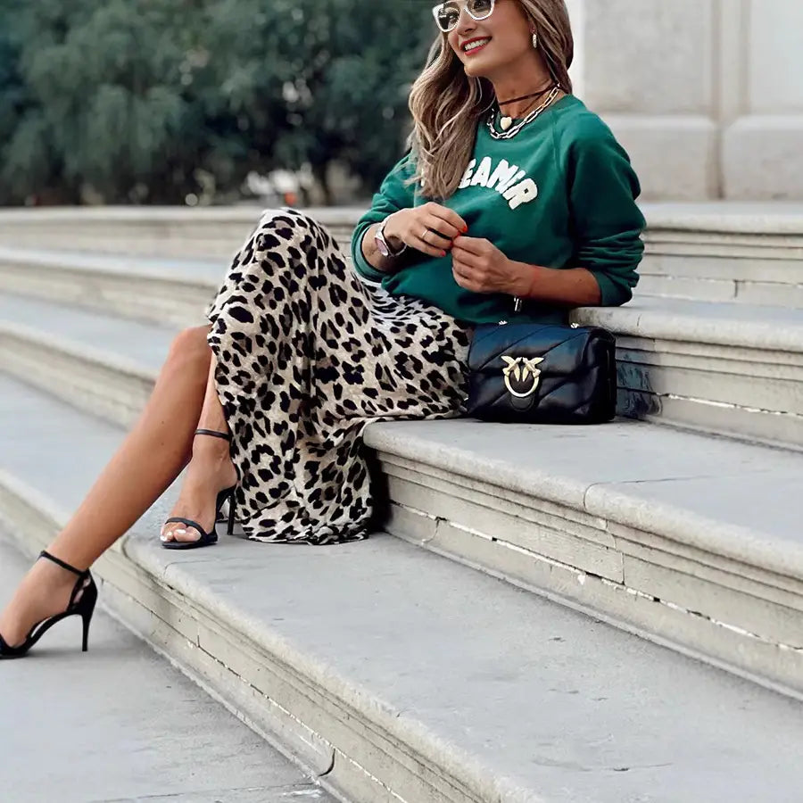 black leather handbag with a gold-tone bird-shaped clasp displayed alongside a black and white leopard print elastic a line skirt