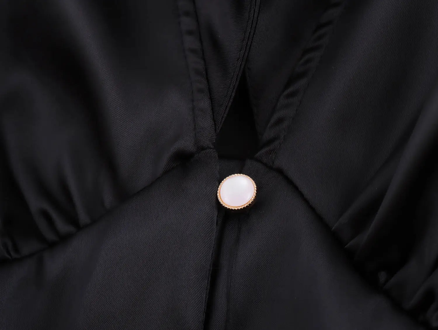 a round pearl-like button with a gold-toned metallic border on the black satin fabric of a white sweet satin dress with fitted waist pleated skirt