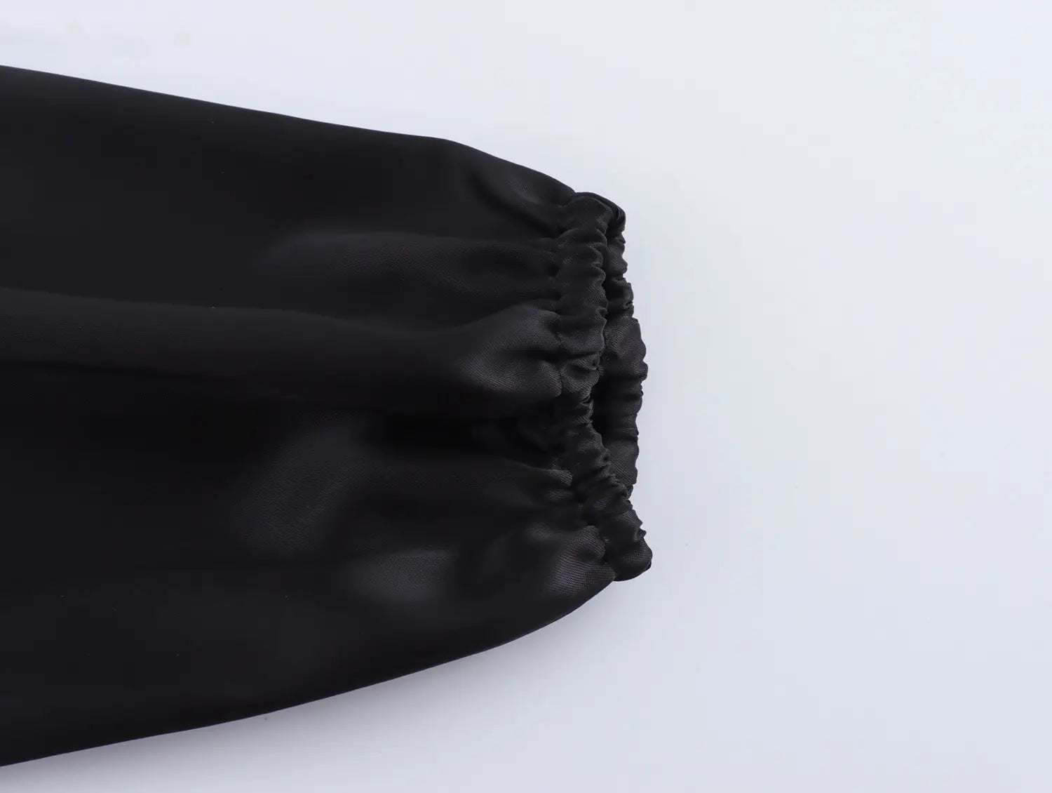 black satin fabric detail with gathered elasticated cuff on a white sweet satin dress featuring a fitted waist pleated skirt