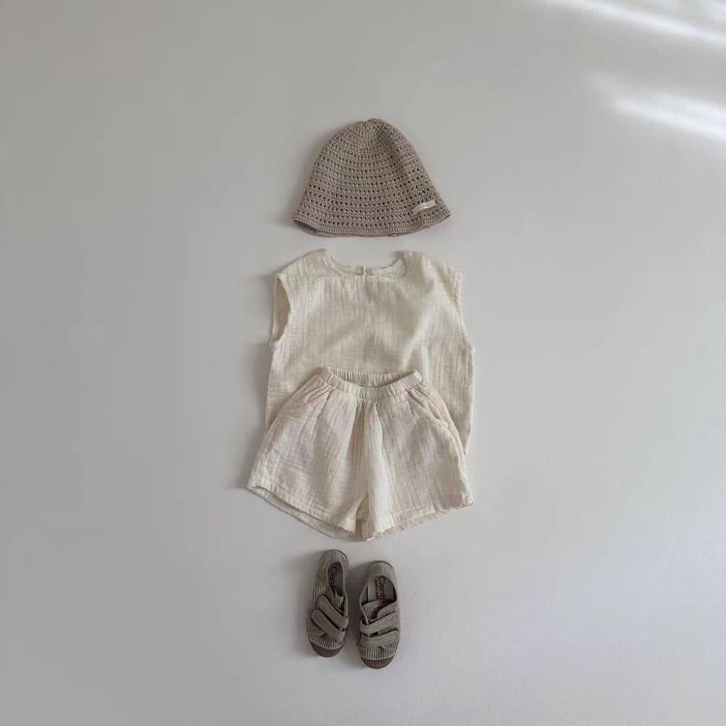beige crocheted bucket hat with small fabric tag on the side paired with a cotton muslin breathable vest shorts set for comfortable summer wear