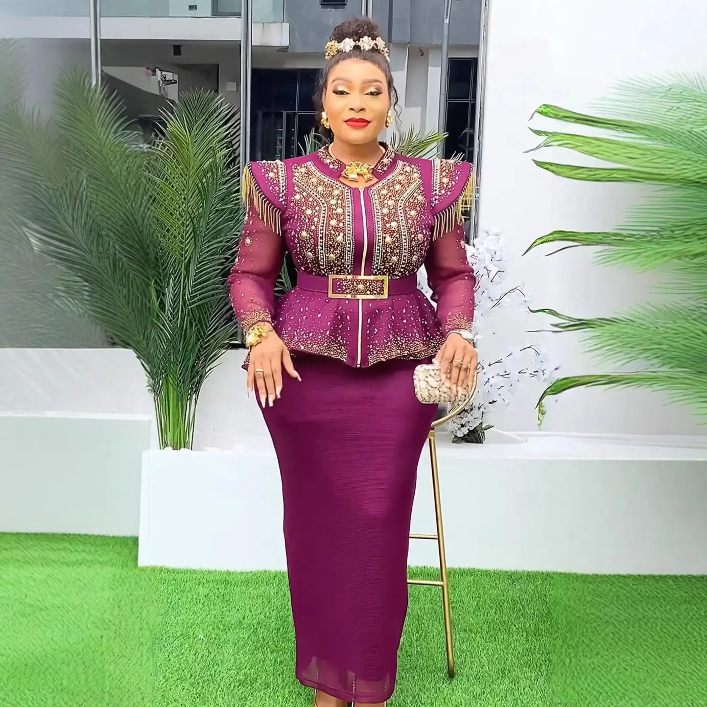 A woman wearing a vibrant purple and gold embroidered solid color hot drilling plus size two piece set with sheer sleeves, peplum waistline, and matching belt.