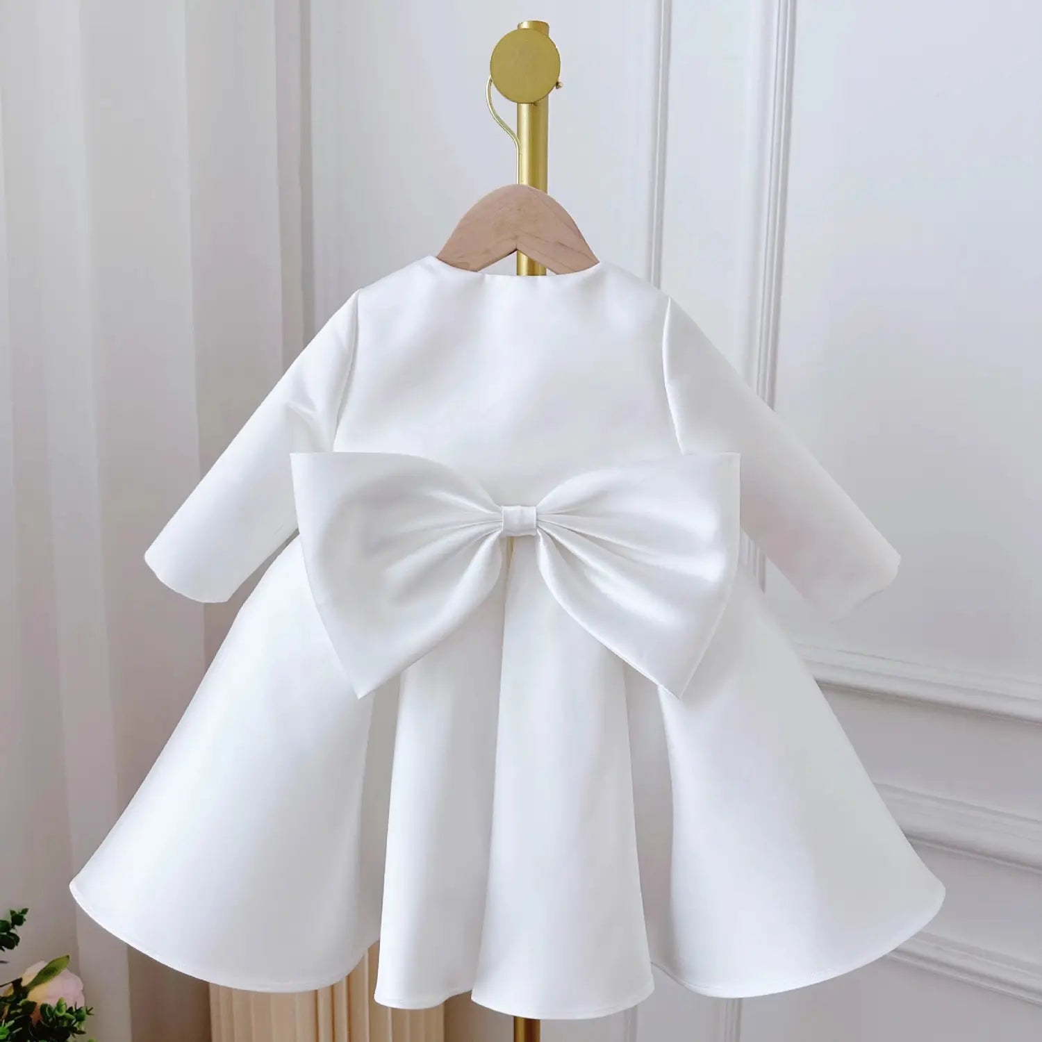 the back of a baby dress white classic style featuring a white satin bow accentuating the long-sleeved white satin dress