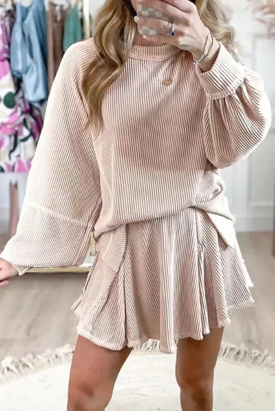 A soft blush pink ribbed knit women’s solid colour casual suit featuring a loose-fitting top with bell sleeves and a flared skirt tied at the waist.