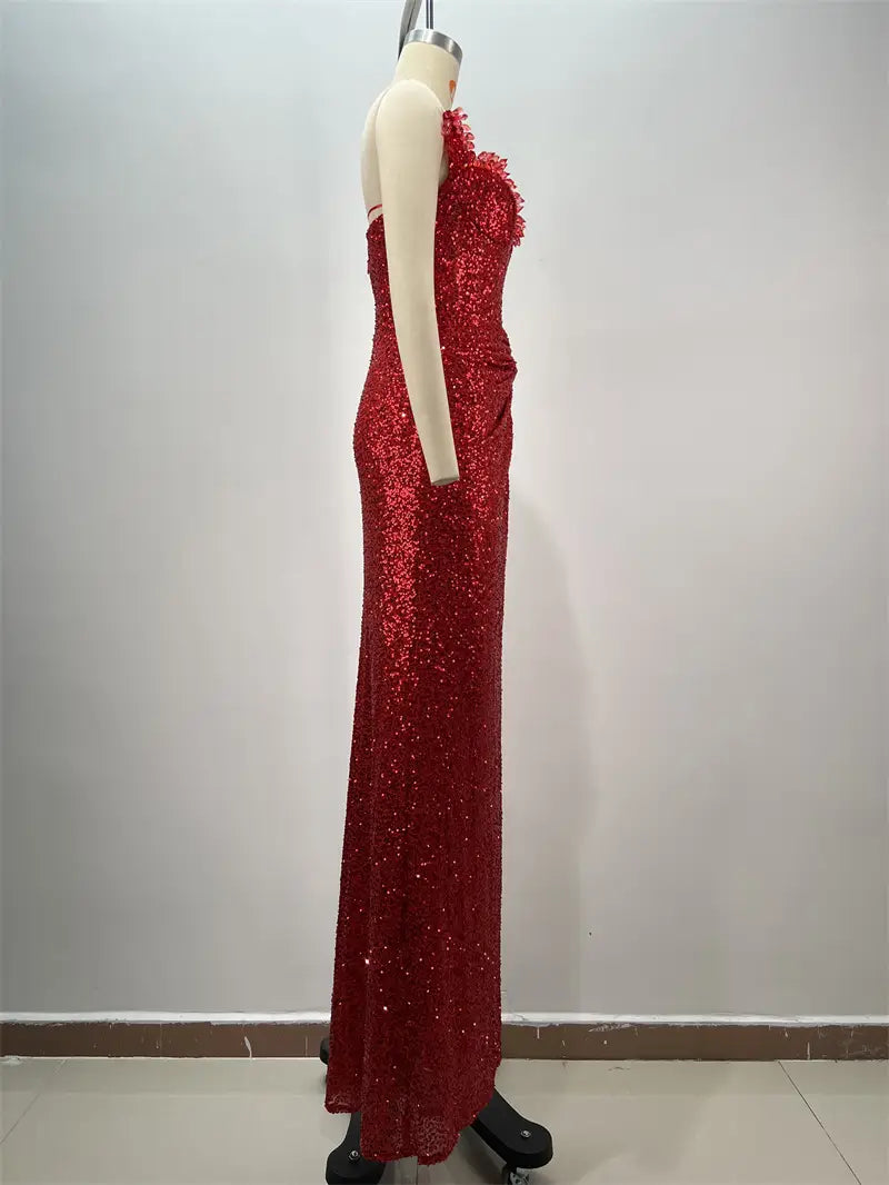 A shimmering red paillette tube evening gown with a one-shoulder design, intricate ruffled neckline detailing, and a form-fitting silhouette featuring a high slit.