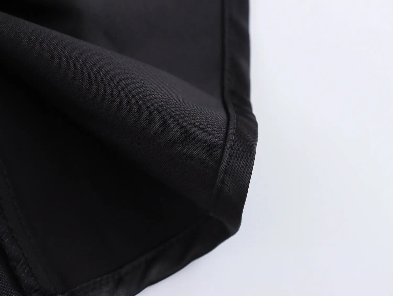 black fabric with a smooth slightly glossy finish and neatly stitched hem on the waist pleated skirt of a white sweet satin dress with fitted waist