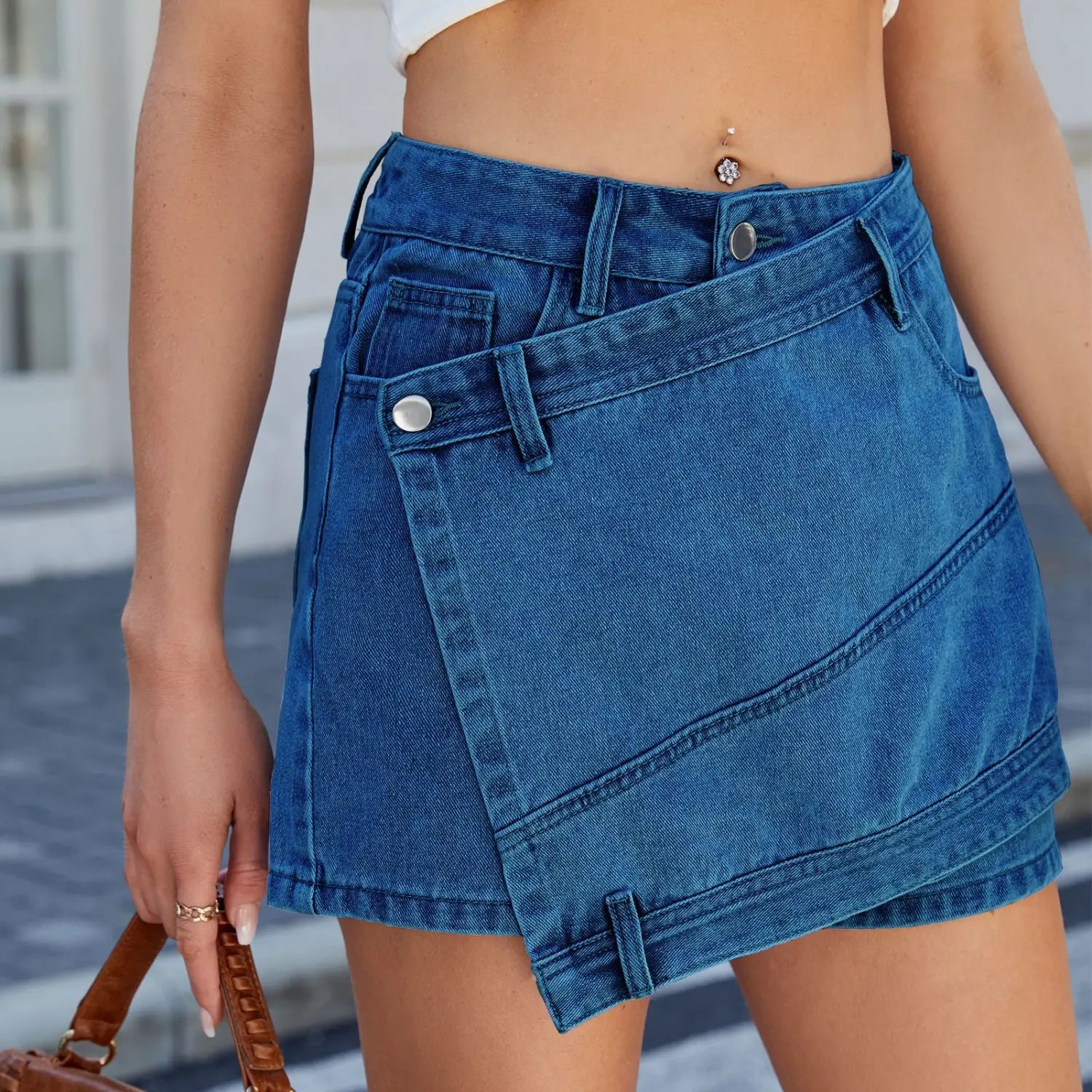 high waist washed irregular denim short skirt in blue featuring a diagonal flap pocket and silver-toned button closures on a denim short skirt.