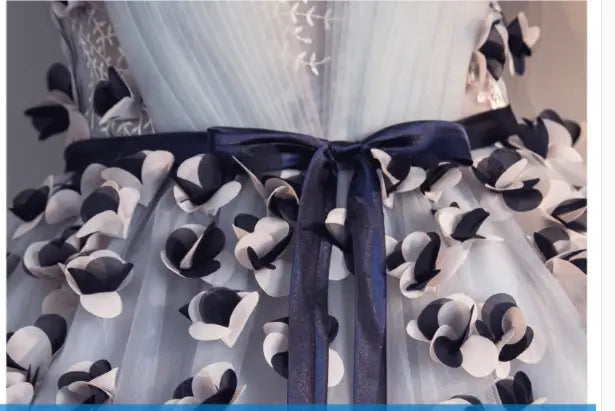 a delicate light blue tulle long skirt with black and white paper-like floral appliqués and a navy satin ribbon bow, designed for vocal choral art and choral art exam performances