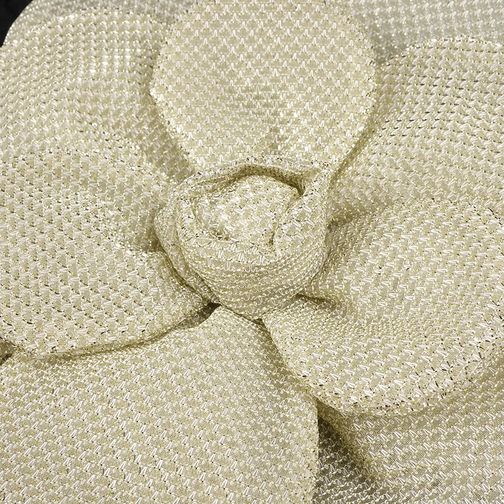 a delicate cream-colored woven fabric flower with a textured shimmering surface and softly folded petals on a black camisole backless slim fit velvet floral gown.